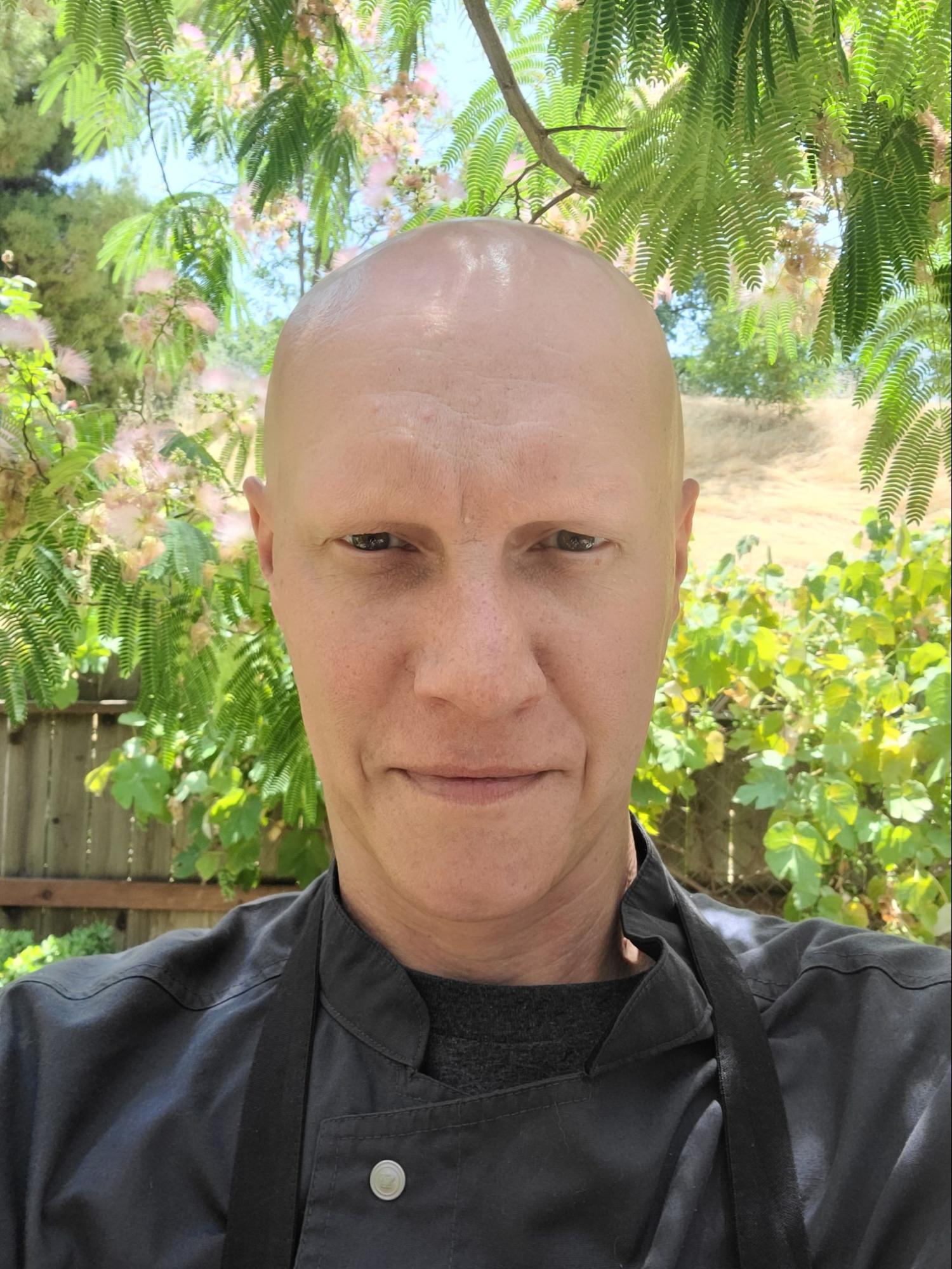 Person in a black shirt outdoors with green plants in the background.