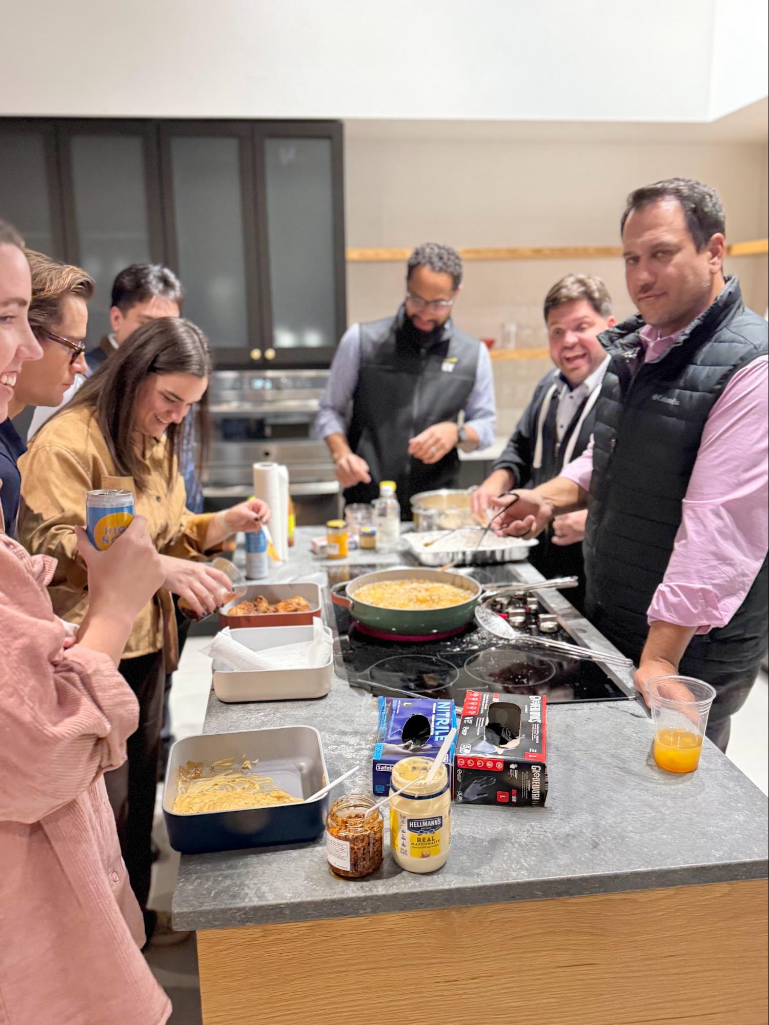 Group cooking together in kitchen around stove with food and condiments on counter.