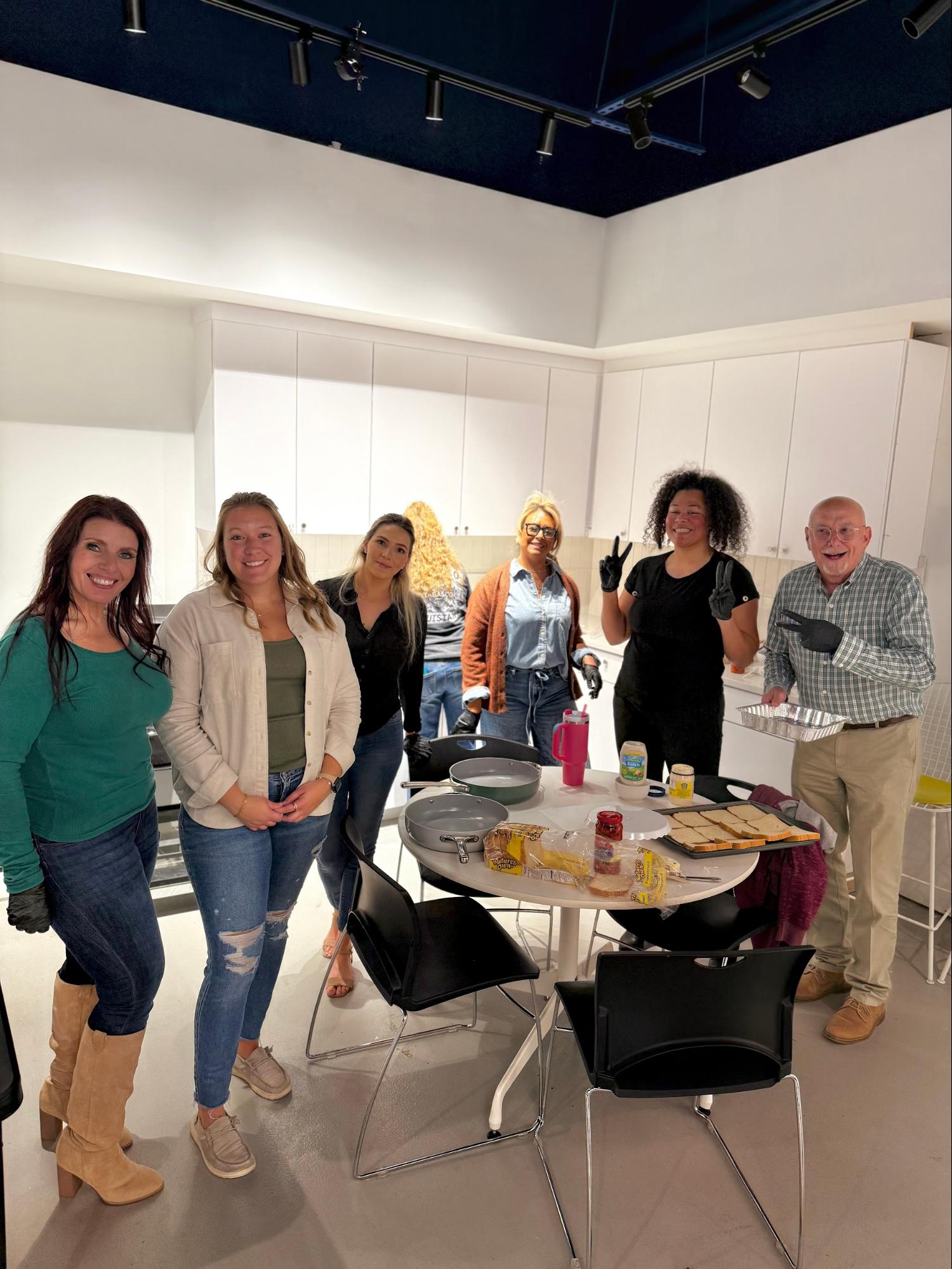 Group of people smiling in a kitchen with food items on a table.