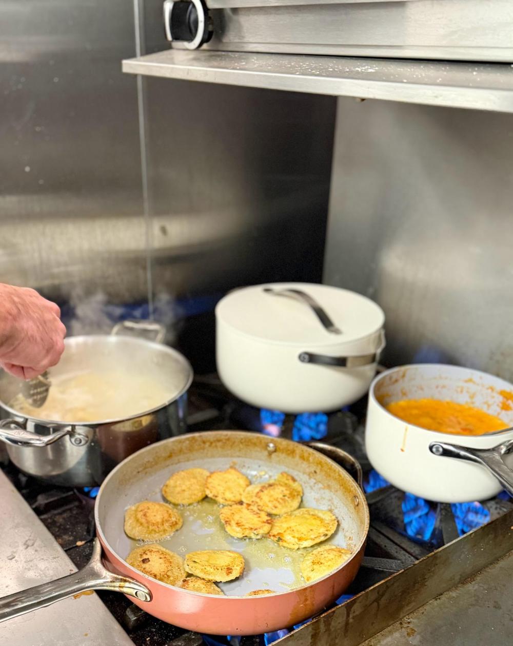 Person cooking fried food in a pan on a stove with pots.