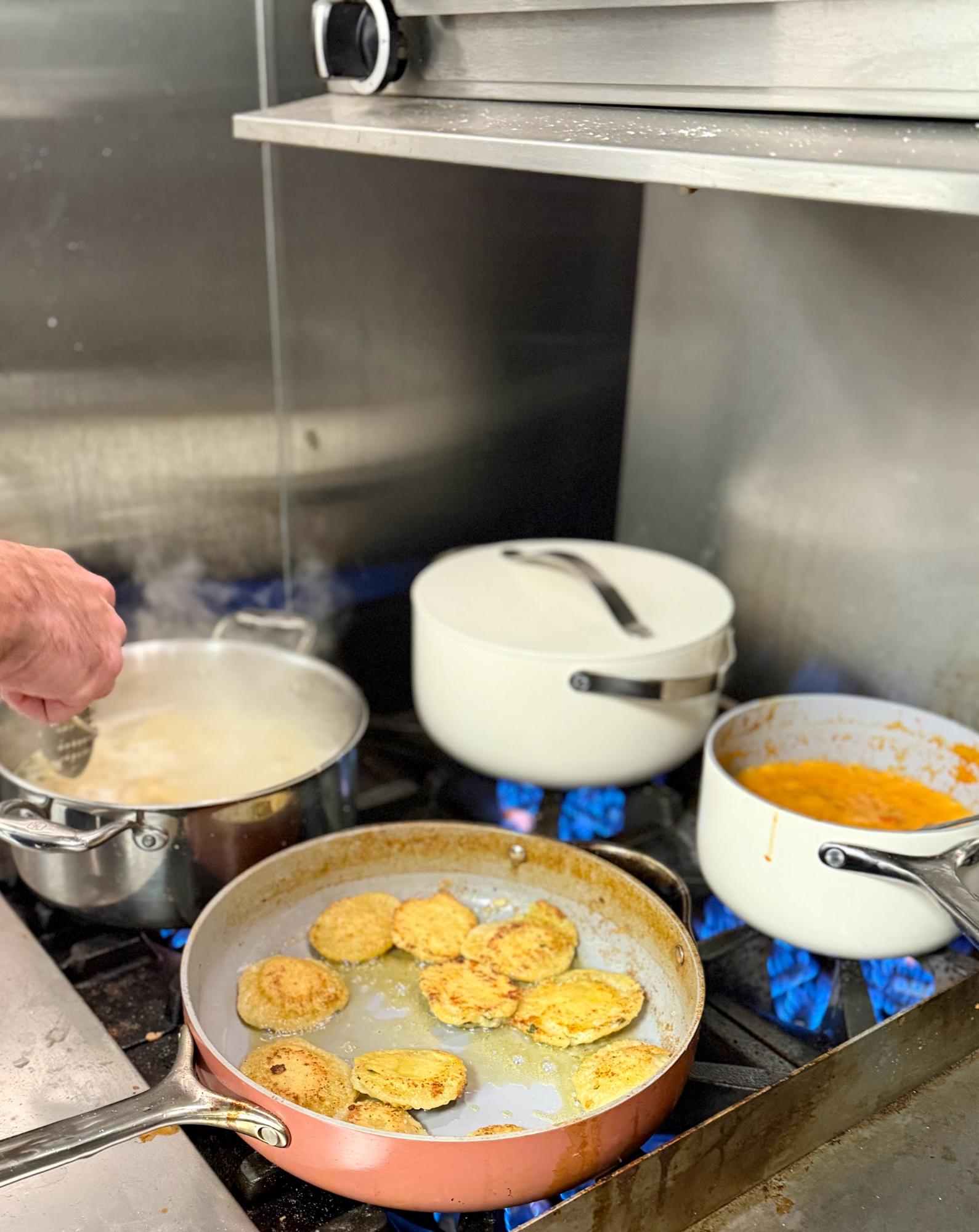 Person cooking fried food in a pan on a stove with pots.