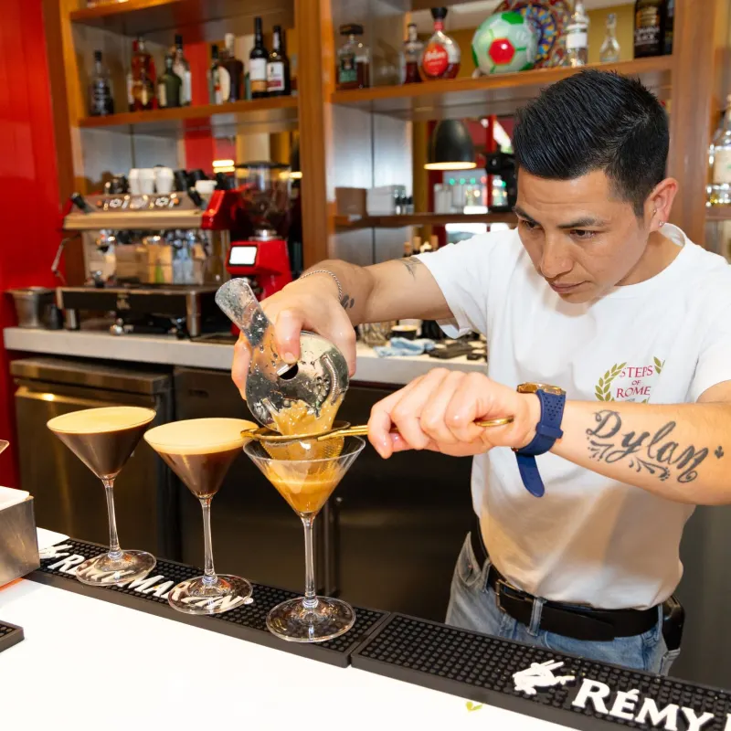 Bartender pouring cocktails into martini glasses at a bar.