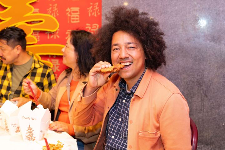 People eating Chinese food, smiling, with a festive red background.