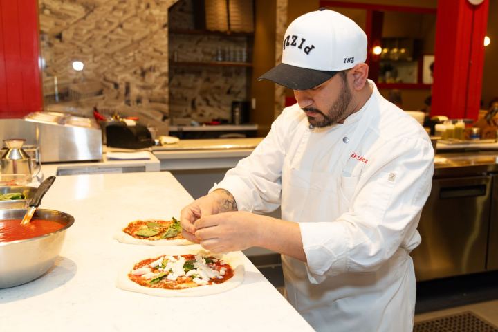 Chef prepares pizzas with toppings in a kitchen setting.