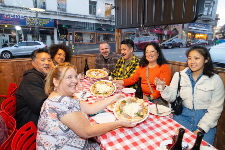 Group of people smiling at a restaurant table with food and drinks.