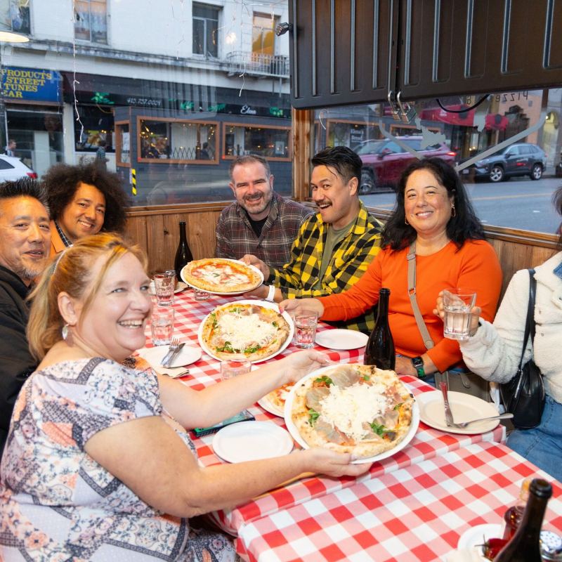 Group of people smiling at a restaurant table with food and drinks.