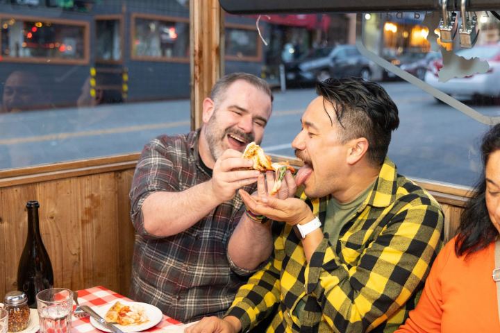 Two people in a restaurant joyfully sharing a slice of pizza.