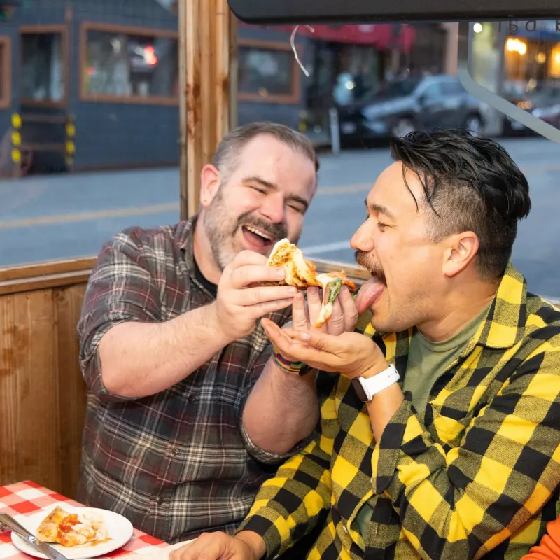 Two people in a restaurant joyfully sharing a slice of pizza.