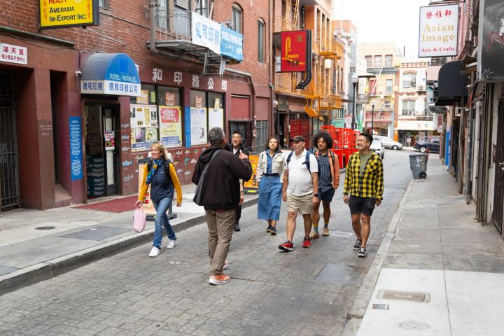 Group of people walking on a narrow city street with shops and signs.