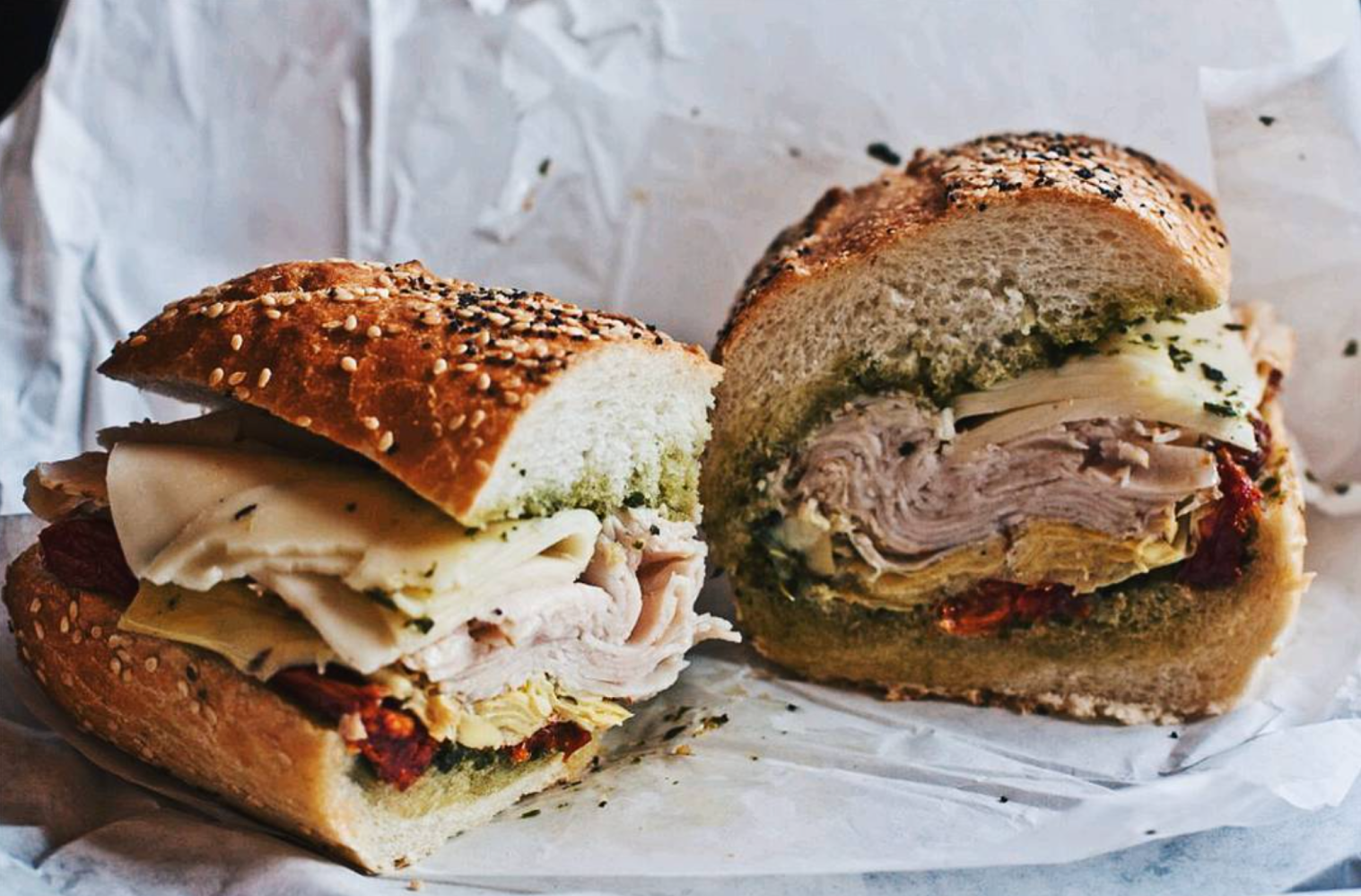 Two halves of a sandwich with turkey, cheese, and vegetables on seeded bread.
